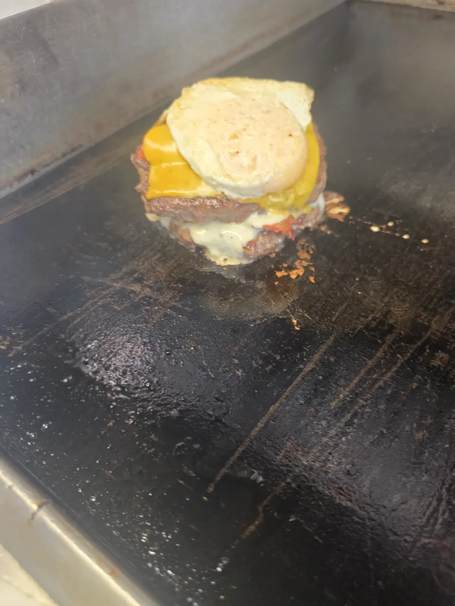 The stack coming together on the griddle: patties, hotlink, cheese, fried egg and the bun crown