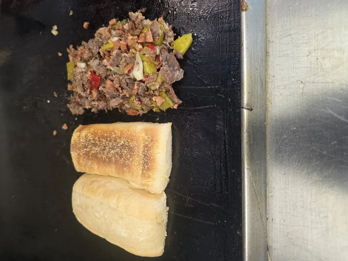 Chopped hotlink and sirloin with Hatch green chile on the flat top, a split hoagie roll toasting beside it