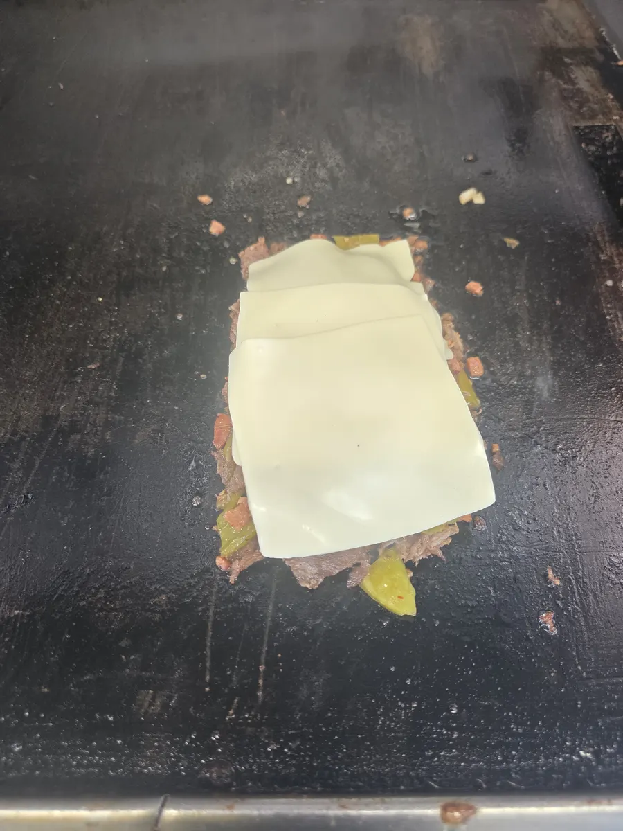 Slices of American Swiss laid over the chopped hotlink and sirloin on the griddle