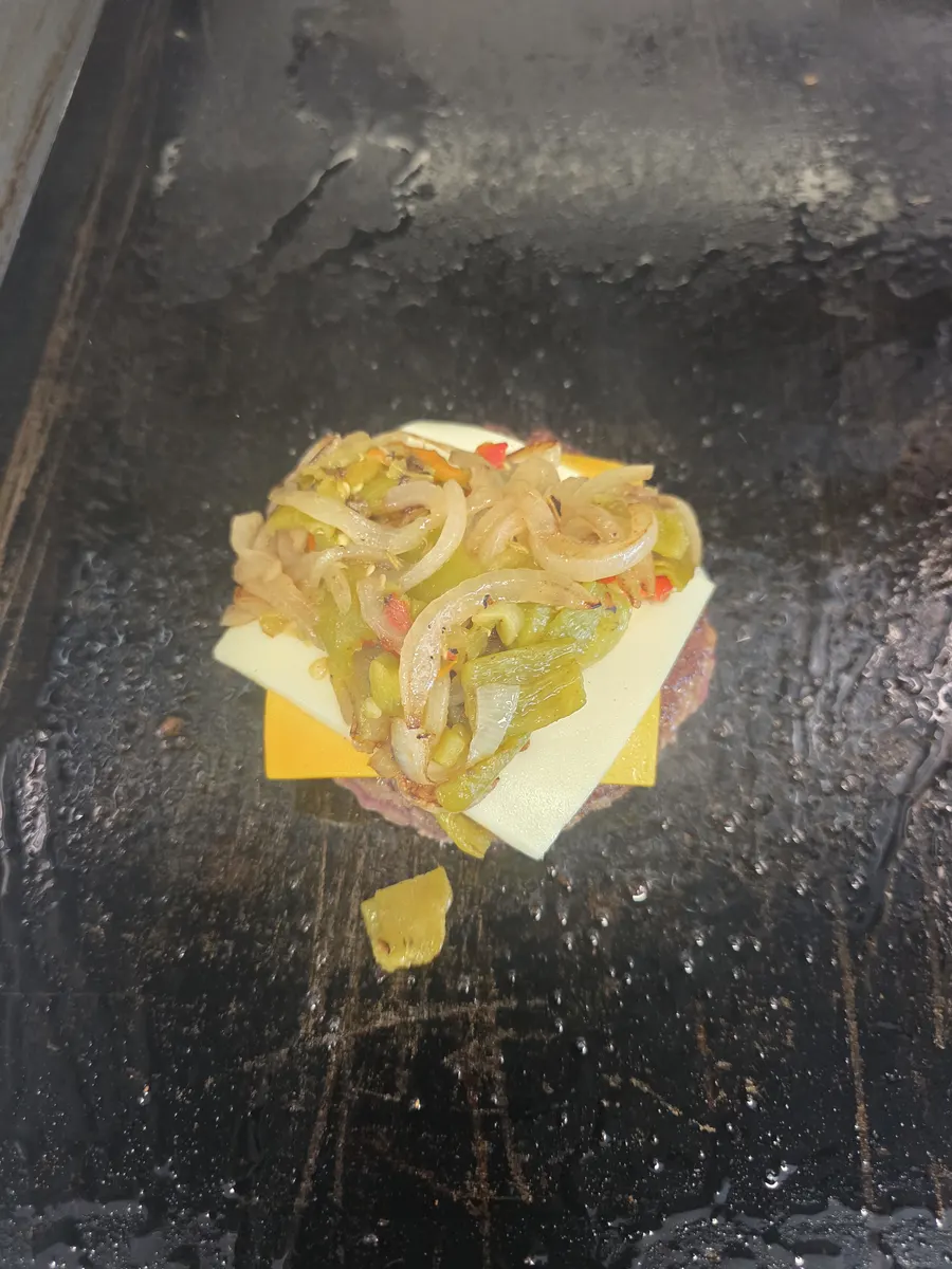 Cheese slices melting on the patty under a pile of Hatch green chile and grilled onions