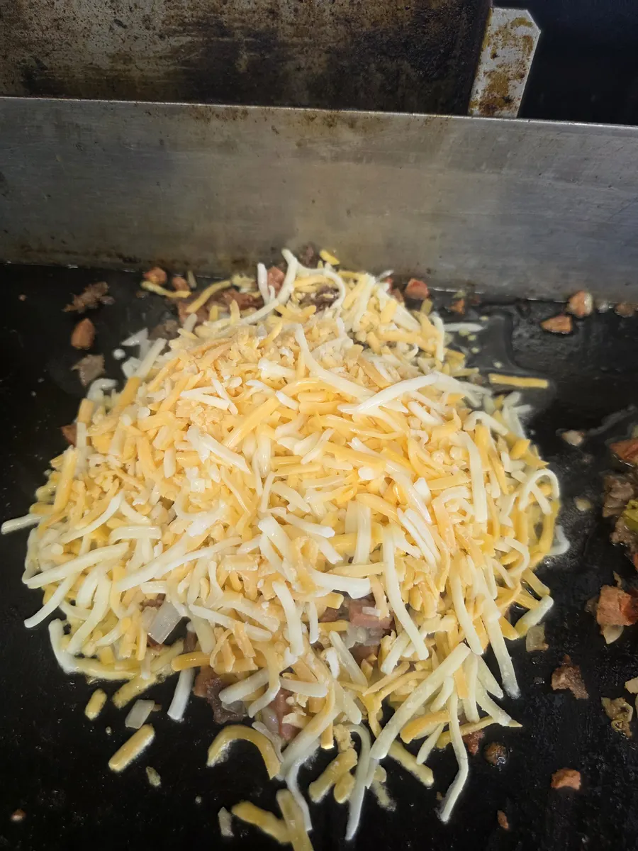 Shredded cheese melting over chopped sirloin and hotlink on the flat top
